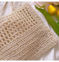 a crocheted bag sitting next to flowers on a bed with white sheets and yellow tulips