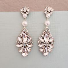 a pair of earrings with pearls and crystal stones on top of a gray surface next to a pink wall