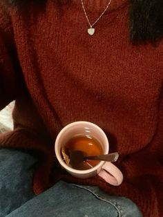 a woman holding a cup of tea in her lap and wearing a heart shaped necklace