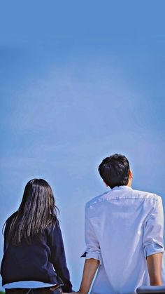 two people sitting on the ground looking at an airplane flying in the sky above them