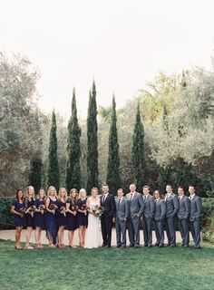 a group of people standing next to each other in front of trees and bushes at a wedding