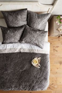 a bed with grey and white comforter on top of it next to a plant