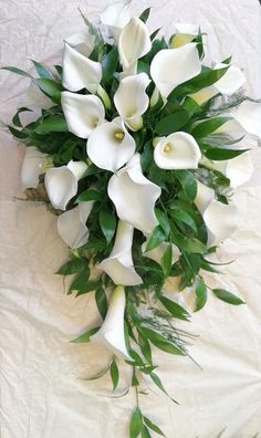 a bouquet of white calla lilies and greenery on a tableclothed surface