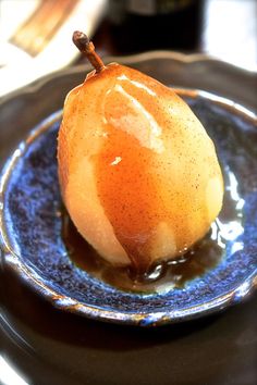 a pear is sitting on a blue plate with caramel sauce in the center and an empty bottle behind it