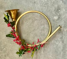 a christmas wreath with holly and bells on the floor next to a gold horn for an xmas ornament