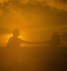 two people holding hands in front of the sun with their arms spread out to each other