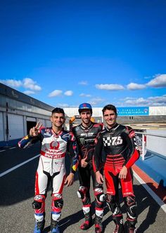 three men standing next to each other on a race track with their motorbikes