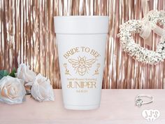 a white coffee cup sitting on top of a table next to flowers and a wreath