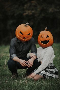 two people sitting in the grass with pumpkins on their heads