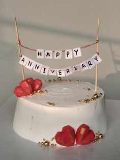 a white cake with red roses on top and happy anniversary banner hanging from it's side