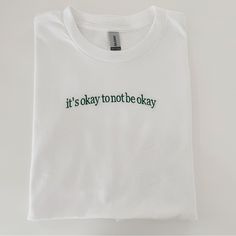 It’s Okay To Not Be Okay White T-shirt With Embroidered Logo For Spring, White Casual T-shirt With Embroidered Text, Casual White T-shirt With Embroidered Text, White Embroidered Text T-shirt For Spring, Everyday White Embroidered T-shirt, Trendy White Embroidered T-shirt, White Embroidered T-shirt For Everyday, White Embroidered T-shirt, White Everyday Top With Embroidered Text