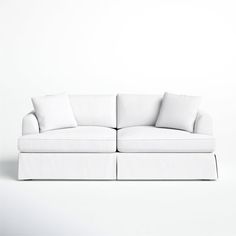 a white couch sitting on top of a white floor next to a wall with two pillows