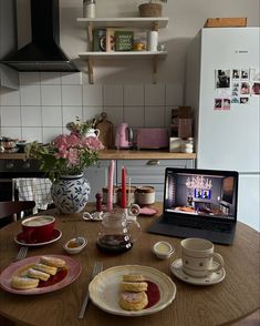 a laptop computer sitting on top of a wooden table next to plates and cups filled with food