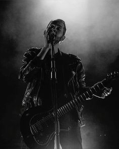 a man holding a guitar while standing in front of a microphone on top of a stage