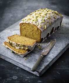 a loaf of cake with frosting and sprinkles next to a knife