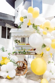 yellow and white balloons are hanging from the side of a table with an old wagon