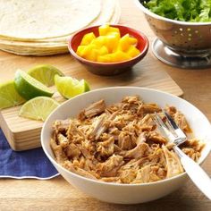 a white bowl filled with shredded meat next to sliced mangoes and tortillas