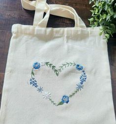 a white bag with blue flowers in the shape of a heart on top of a wooden table