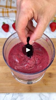 a person is mixing something in a blender on a cutting board with strawberries