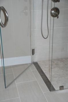 a walk in shower sitting next to a white tiled wall and floor covered in gray tile