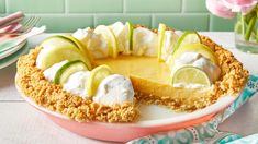 a lemon custard pie with whipped cream and limes on top is sitting on a table