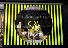 a store front window with yellow and black stripes on the outside, featuring an advertisement for prune outlet sale