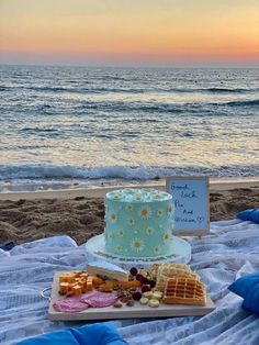 a blue cake sitting on top of a table next to the ocean at sunset or dawn