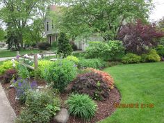 a garden with lots of different types of flowers and plants around it in front of a house