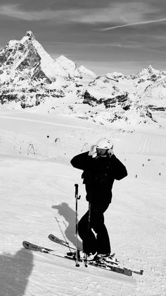 a man riding skis down the side of a snow covered slope with mountains in the background