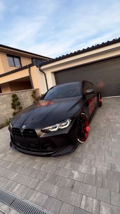 a black car parked in front of a house with red rims on it's tires