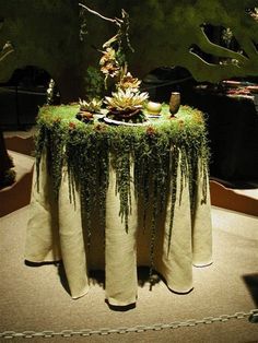 a table covered in plants and greenery on top of a carpeted floor next to a tree