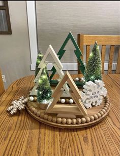 a wooden tray with christmas trees and decorations on top of it, sitting on a dining room table