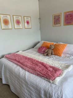 a bed with pink and orange pillows on it in a room that has pictures on the wall