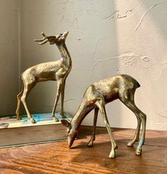 two brass deer statues are standing on a wooden table next to a mirror and book