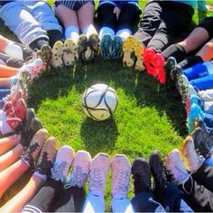 a group of people sitting in a circle around a soccer ball on the grass with their feet up