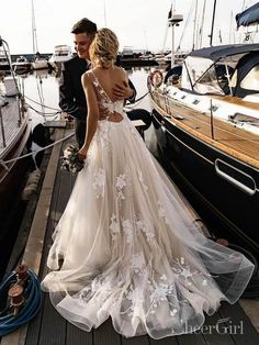 a woman in a wedding dress standing on a dock next to a man wearing a suit