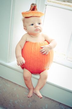 a baby in a pumpkin costume sitting on a window sill