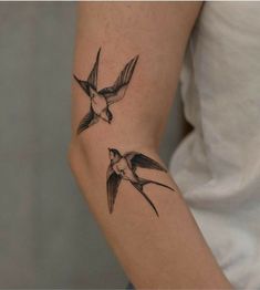 two small birds flying in the air with their wings spread out and one bird is on top of the arm