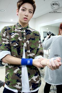 a young man in camouflage shirt and white tie holding onto a wristband with other people behind him