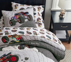 a bed with monster trucks on it in a room next to a night stand and nightstand