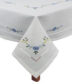 a white table cloth with blue and yellow flowers on the border is sitting on a wooden stand