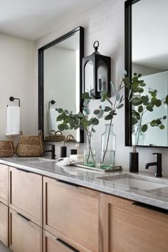 a bathroom with two sinks and mirrors on the wall next to it is a plant in a glass vase