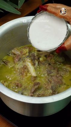 a person pouring milk into a pot filled with food