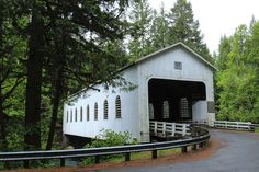 an old white covered bridge in the middle of a wooded area with trees around it