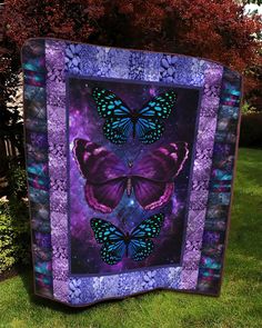 two purple and blue butterflies on a quilted wall hanging in front of some trees