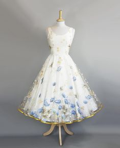 "A striking 1950s style wedding dress made from an embroidered lace featuring huge blue poppies and delicate white and gold daises. It features a darted scoop neck bodice that offers simplicity and a flattering silhouette. The tea length circle skirt is edged with gold satin trim. The dress is made from a layer of lace over an ivory cotton lawn which is then lined.  This dress is ready made and available off-the-peg in a size UK 10 (US 6-8/EU 38). It has been made to fit a waist measurement of 2 1950s Tea Length Wedding Dress, 1950s Wedding Dress Tea Length, Tea Length Formal Dresses, Dig For Victory, Tea Length Wedding, Yule Ball, Tea Length Wedding Dress, Tea Length, Mode Vintage