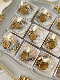 several small square trays with gold and white decorations on them, each containing different type of buttons