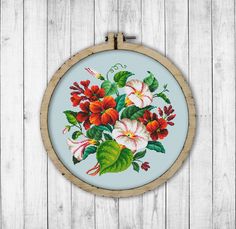 a cross stitch flower arrangement in a wooden hoop on a white wood background with text overlay