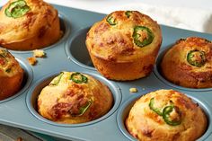 several muffins in a blue tray with green peppers on top and other muffins behind them