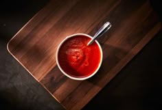 a bowl filled with sauce on top of a wooden cutting board next to a spoon